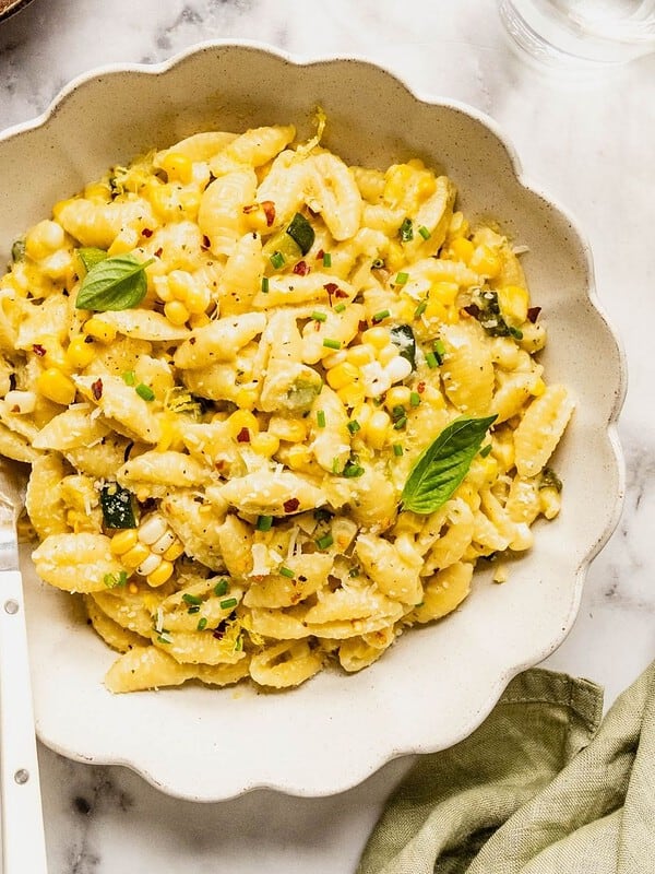 Bowl of creamy corn and zucchini pasta garnished with basil, lemon zest, chili flakes and parmesan.