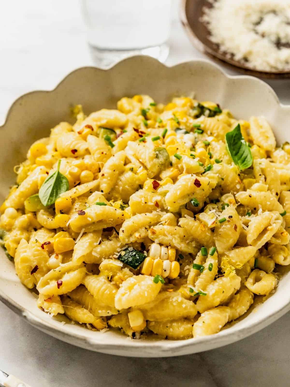 Bowl of creamy corn and zucchini pasta garnished with basil, lemon zest, chili flakes and parmesan.