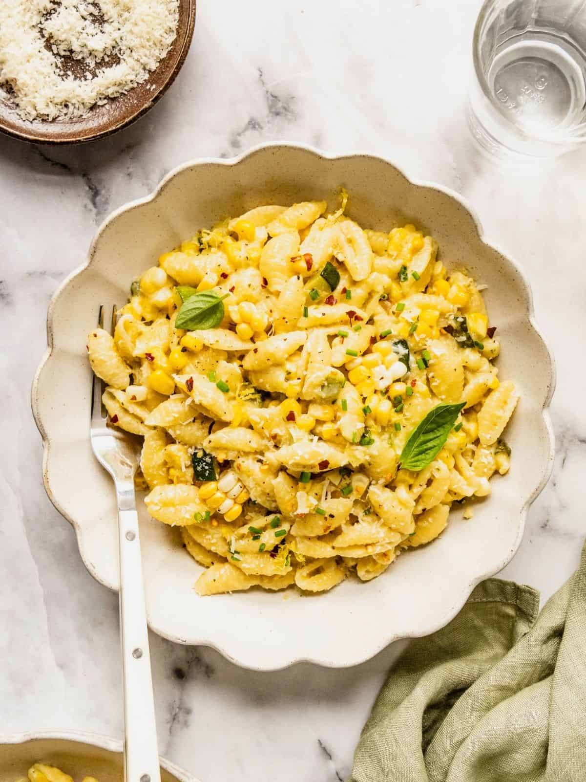 Bowl of creamy corn and zucchini pasta garnished with basil, lemon zest, chili flakes and parmesan.