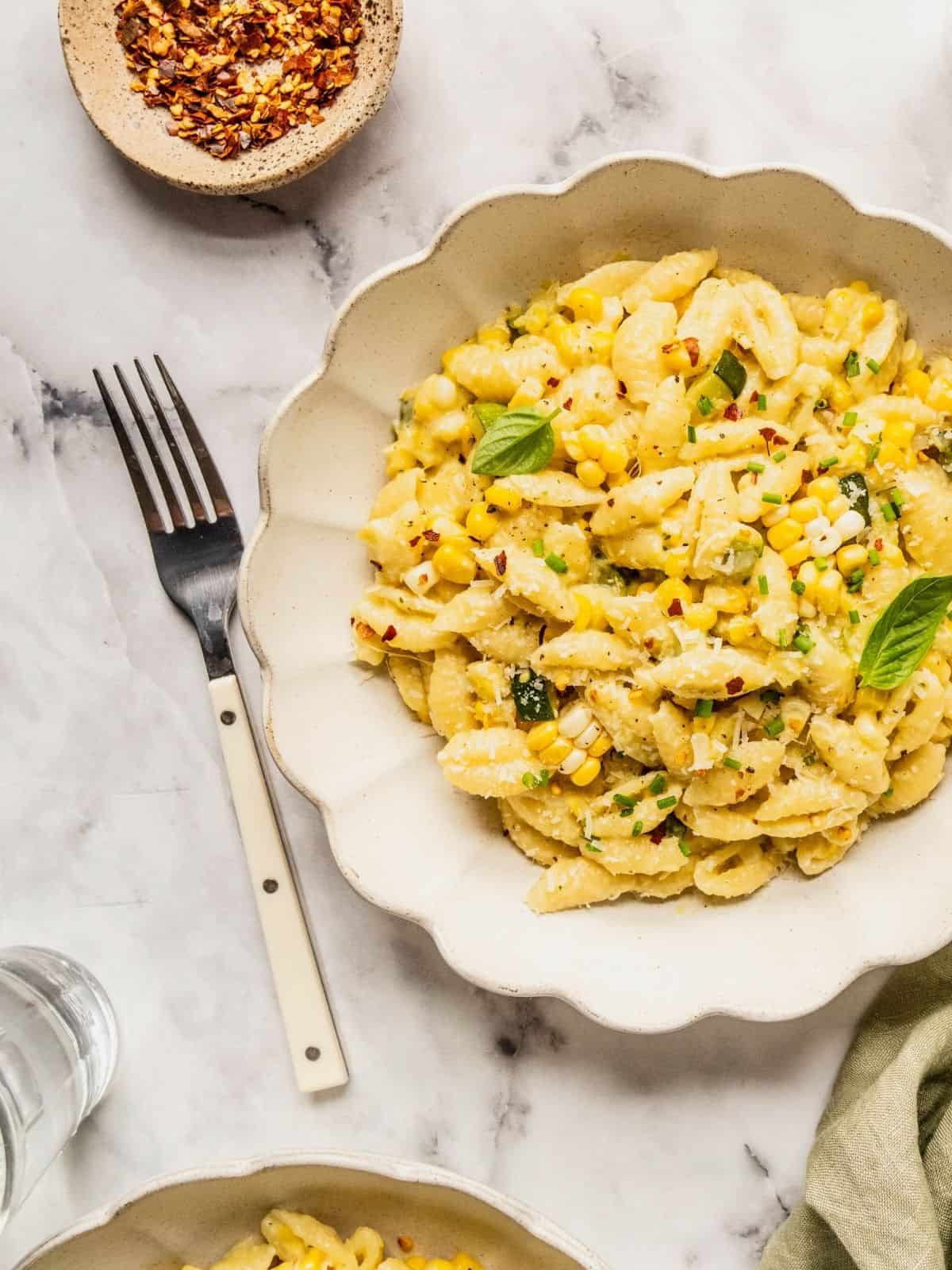 Bowl of creamy corn and zucchini pasta garnished with basil, lemon zest, chili flakes and parmesan.