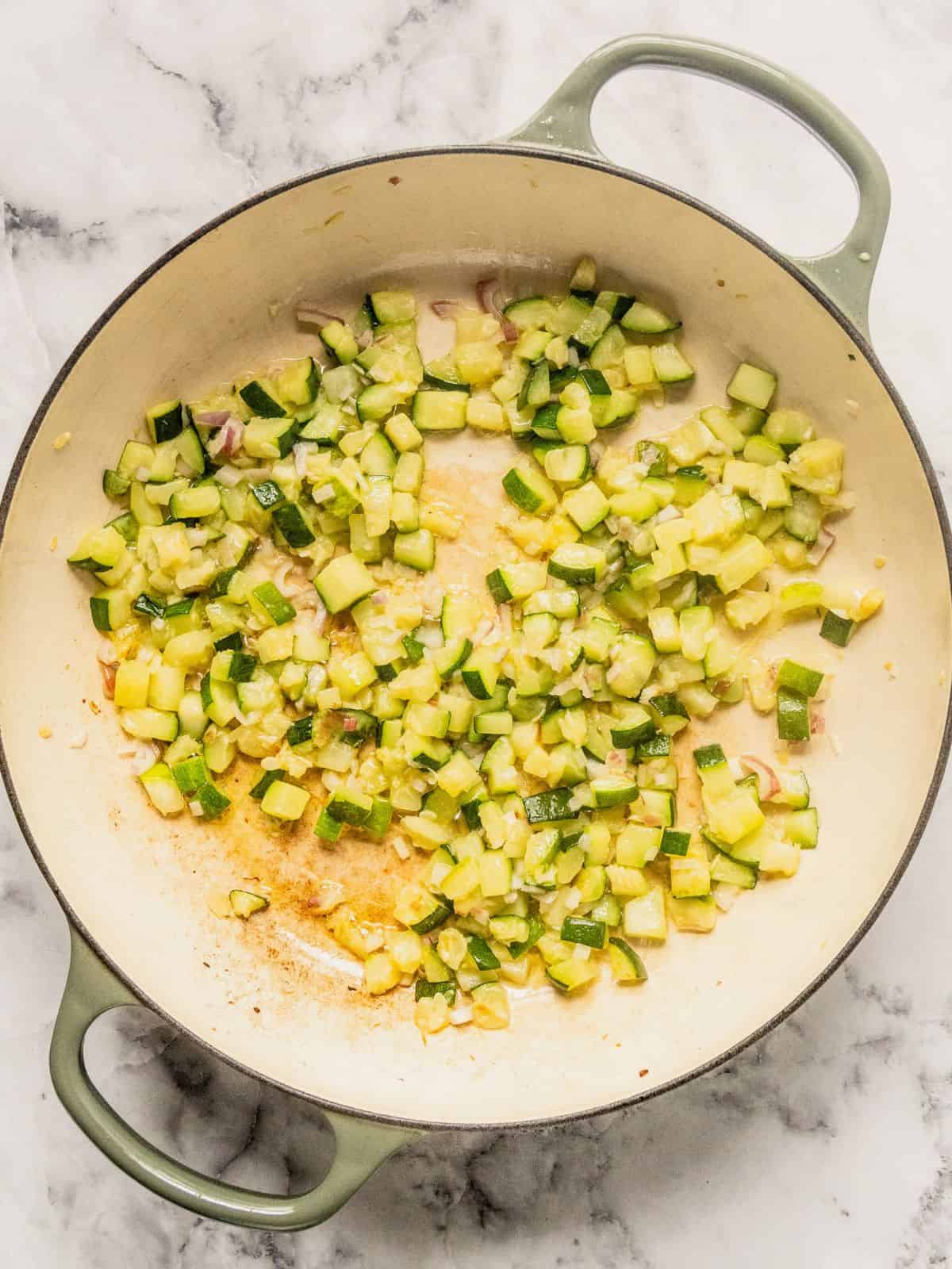 Zucchini, shallots and garlic frying in a large cast iron saucepan.