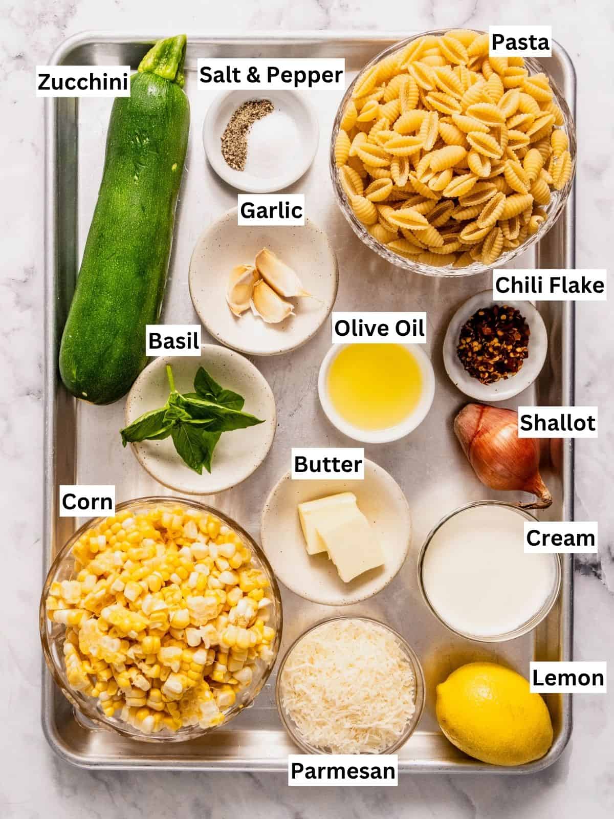 Creamy corn and zucchini pasta recipe ingredients with individual labels on a metal tray.