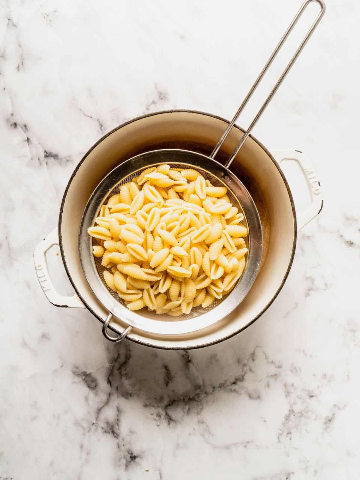 Small pasta draining in a sieve over a pot.