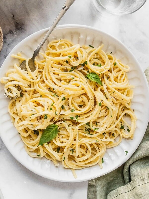 Bowl of creamy pasta al limone garnished with herbs and Parmesan.