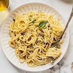 Bowl of creamy pasta al limone garnished with herbs and Parmesan.