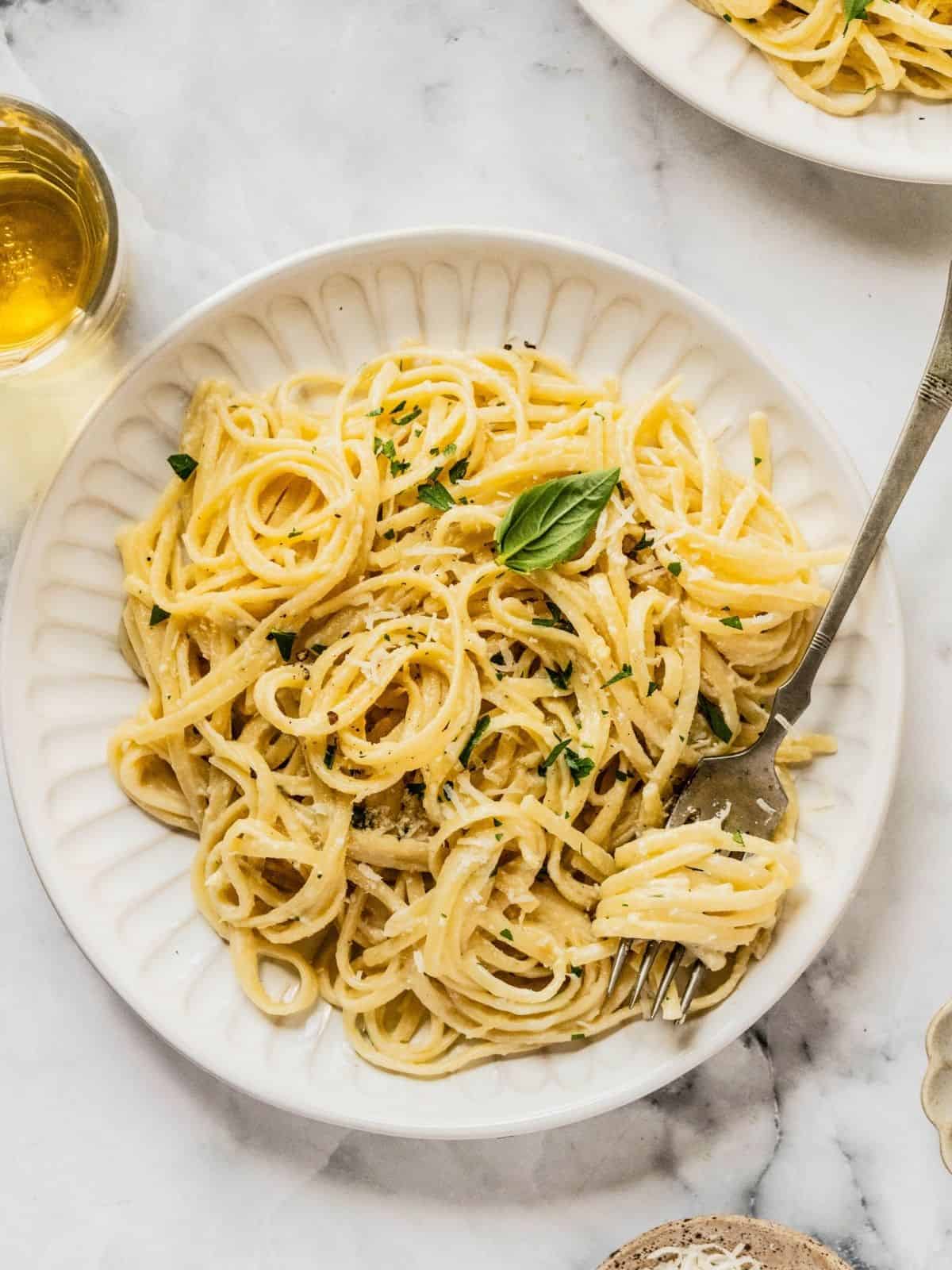 Bowl of creamy pasta al limone garnished with herbs and Parmesan.