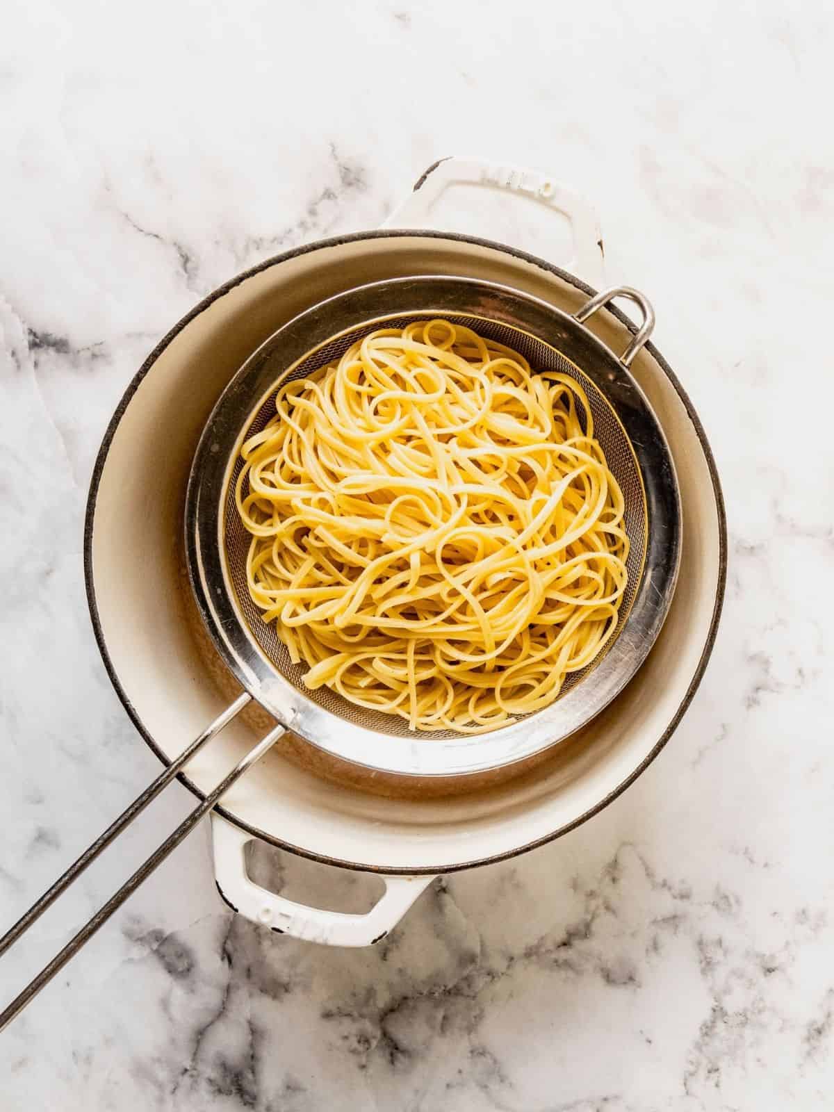 Pasta draining in a sieve over a pot.