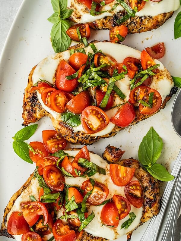 Platter with grilled chicken margherita garnished with cherry tomatoes and basil.