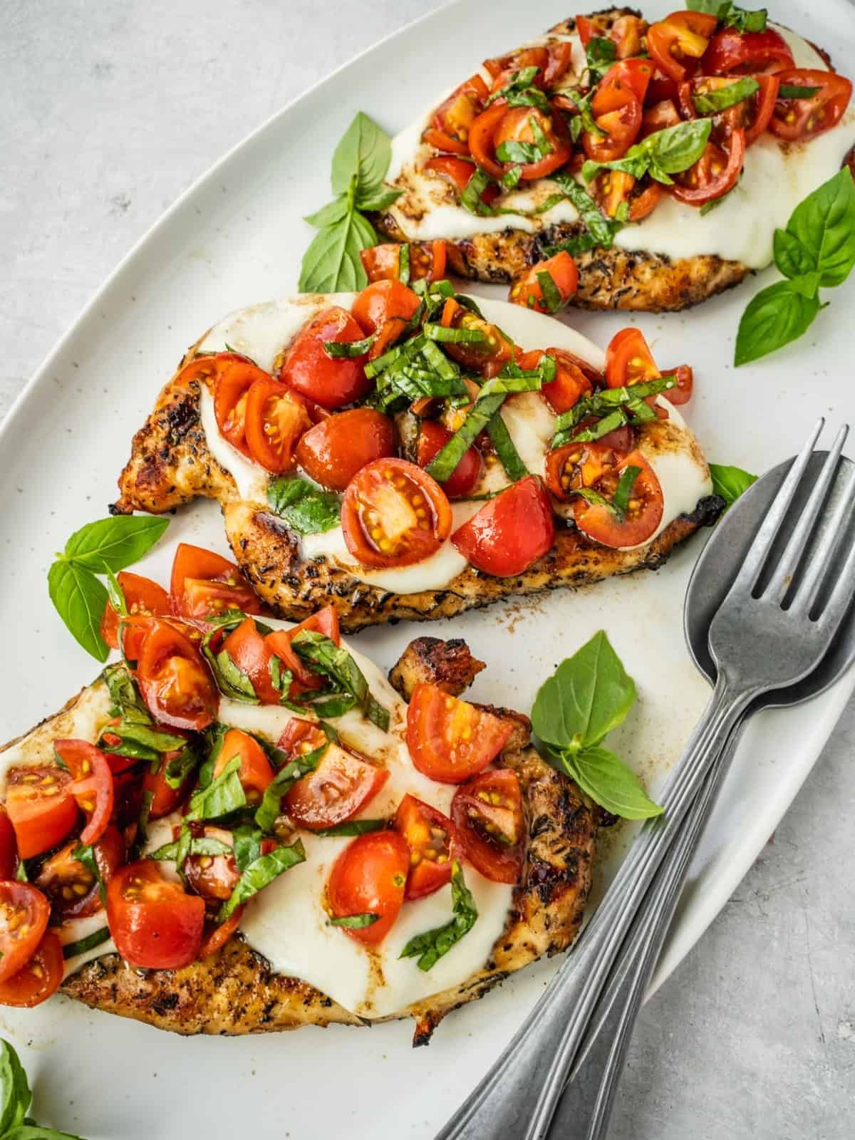 Platter with grilled chicken margherita garnished with cherry tomatoes and basil.