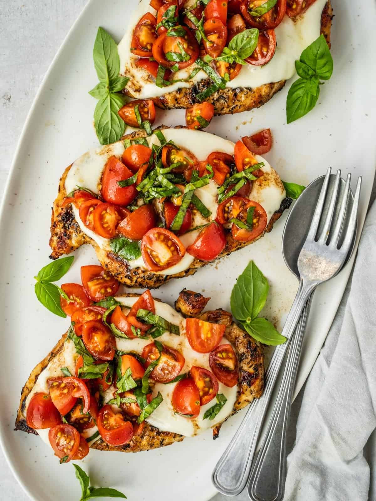 Grilled chicken margherita on a platter garnished with cherry tomatoes and basil.