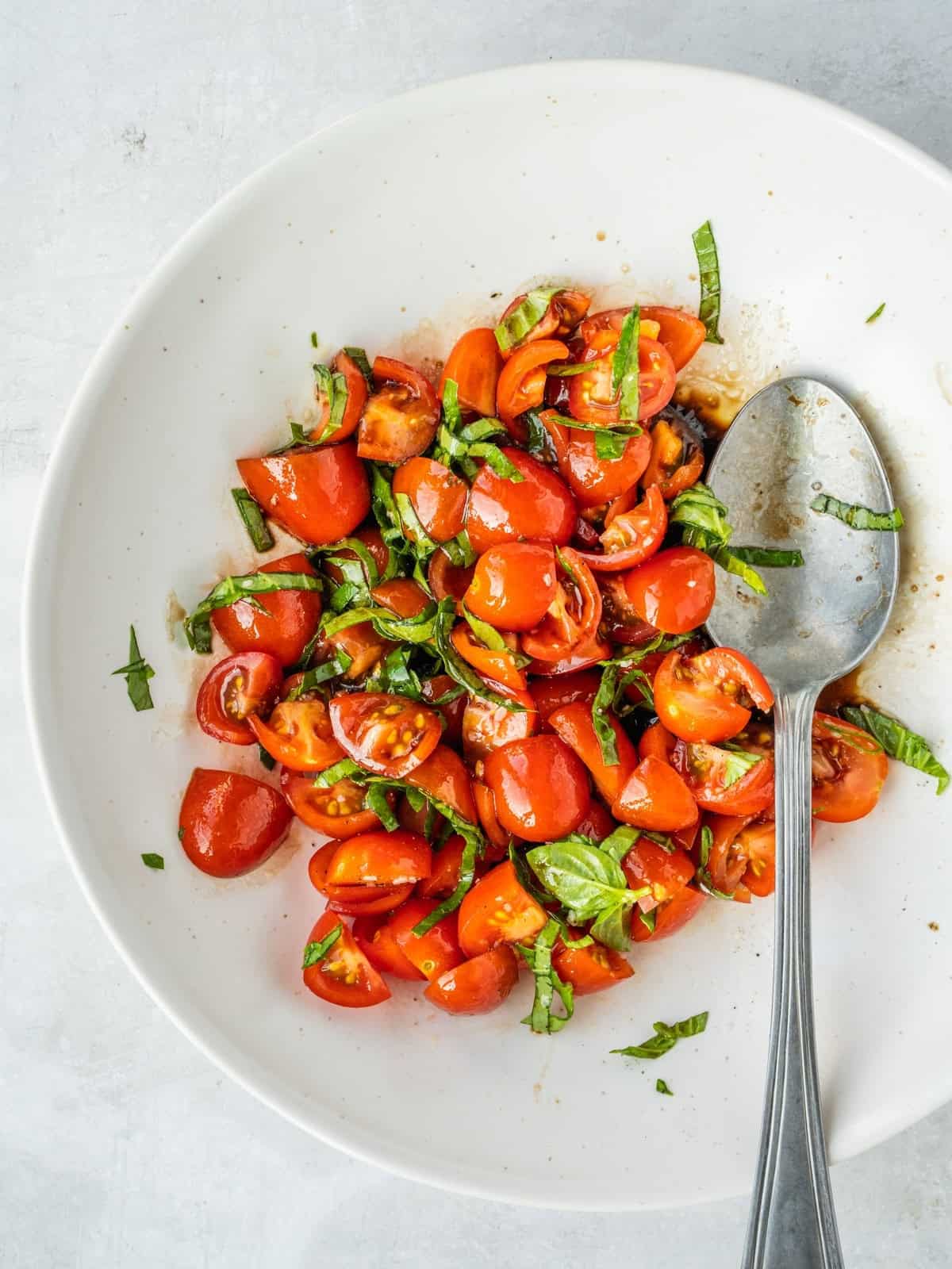Bowl with sliced cherry tomatoes, torn basil, olive oil, balsamic vinegar, garlic, salt and pepper.