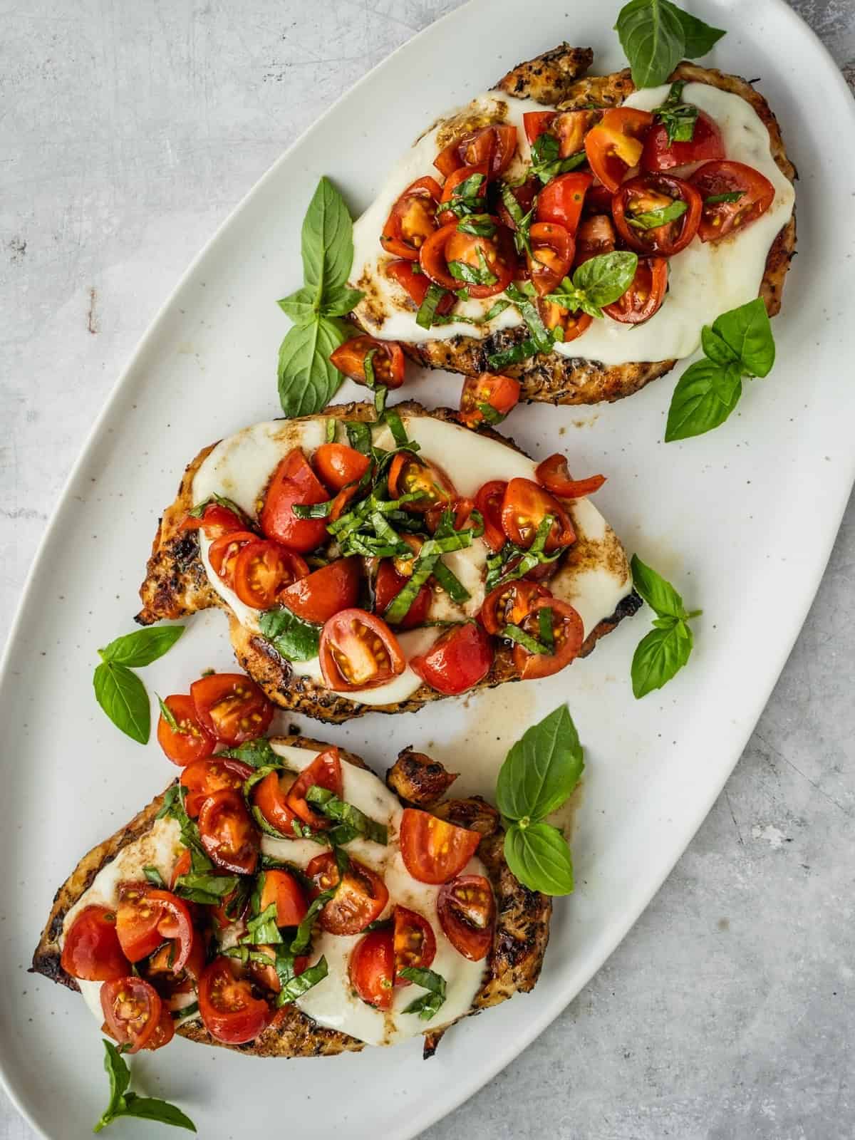 Platter with grilled chicken margherita garnished with cherry tomatoes and basil.