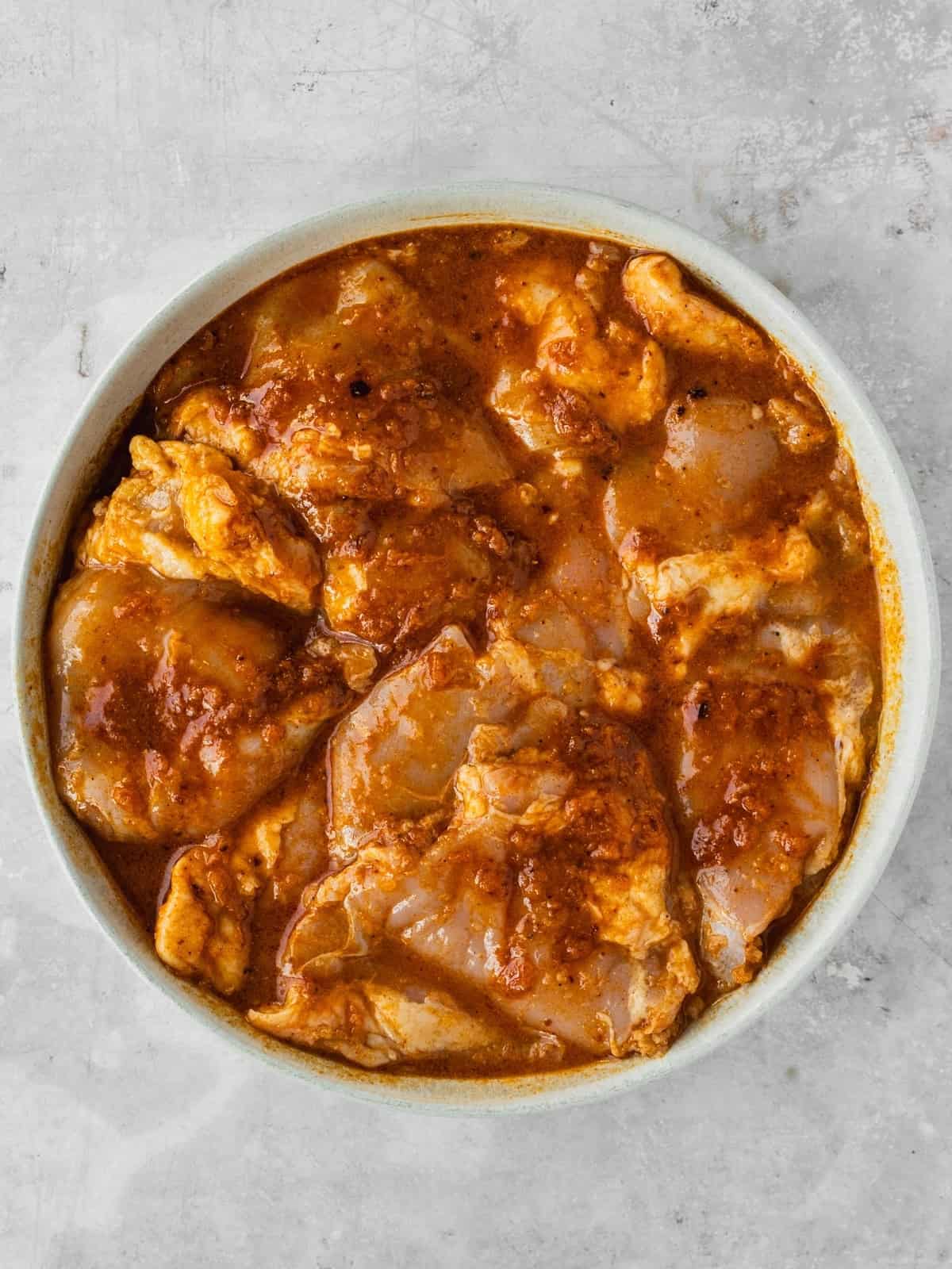 Chicken thighs marinating in the piri piri chicken marinade in a bowl.