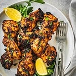 Grilled piri piri chicken thighs on a platter garnished with parsley and lemon wedges.