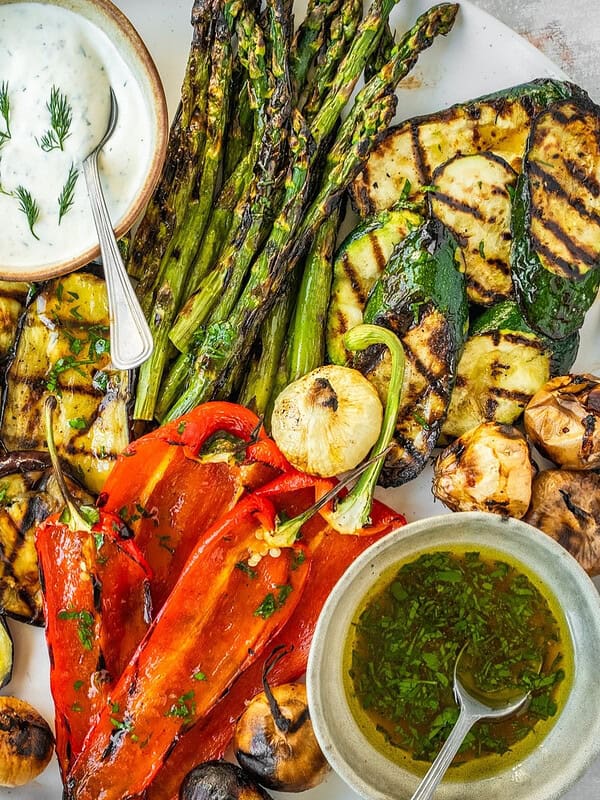 Grilled vegetables including asparagus, zucchini, eggplant and peppers on a platter with two sauces, one creamy and one oily.