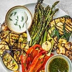 Grilled vegetables including asparagus, zucchini, eggplant and peppers on a platter with two sauces, one creamy and one oily.