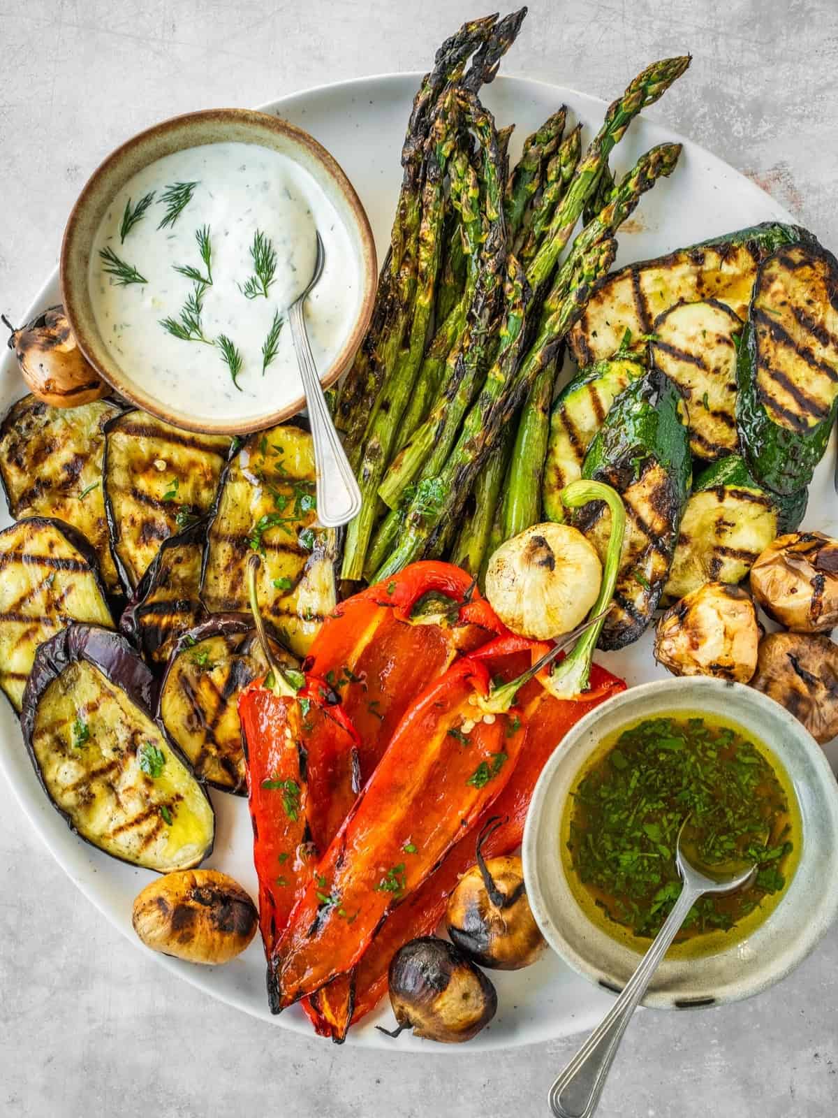 Grilled vegetables including asparagus, zucchini, eggplant and peppers on a platter with two sauces, one creamy and one oily.
