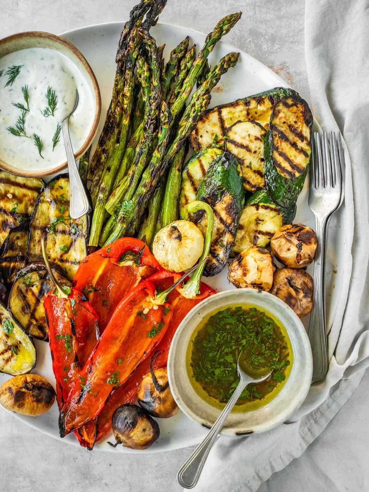 Grilled vegetables including asparagus, zucchini, eggplant and peppers on a platter with two sauces, one creamy and one oily.