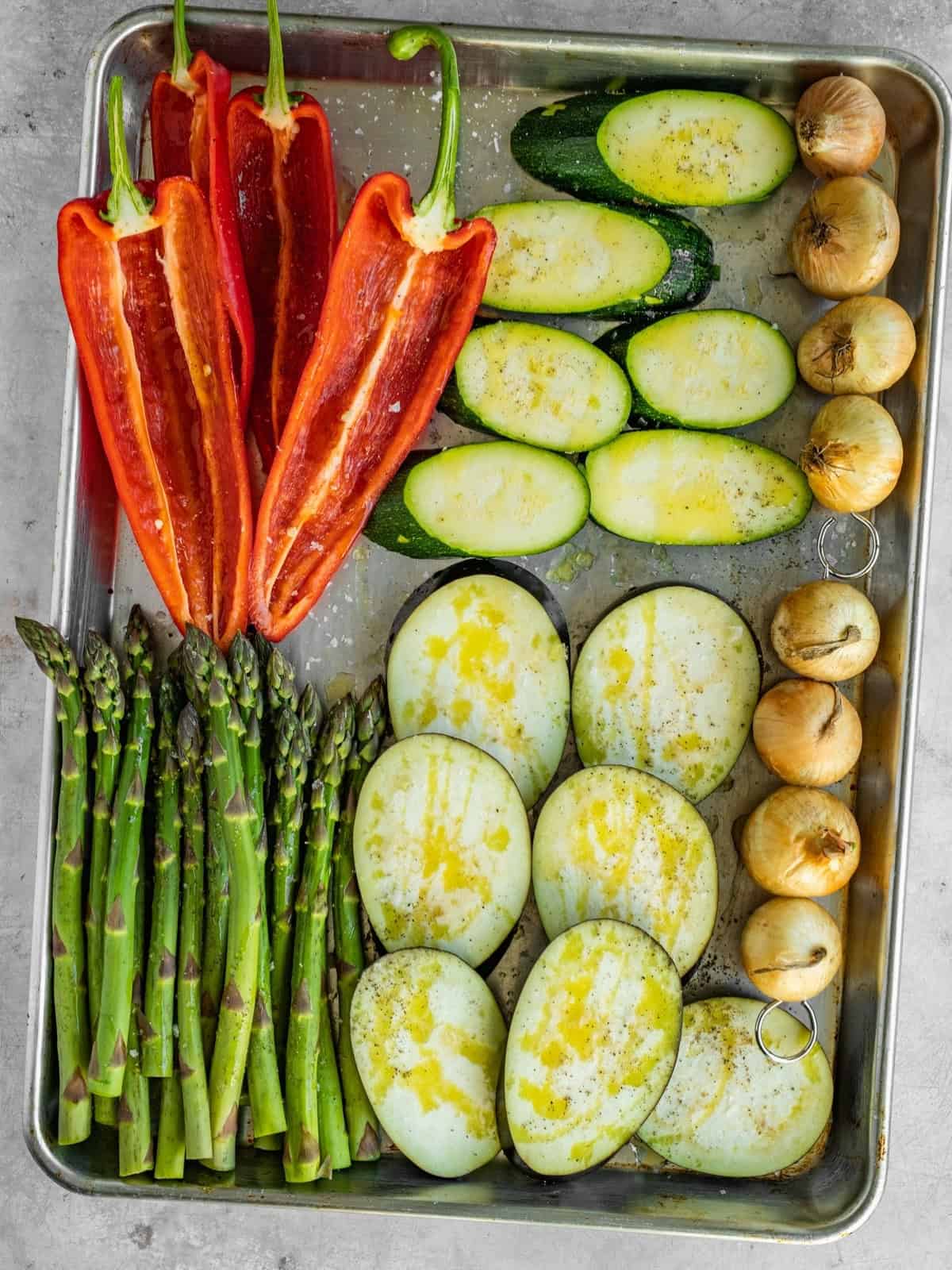 Seasoned sliced vegetables on a metal tray waiting to be grilled.