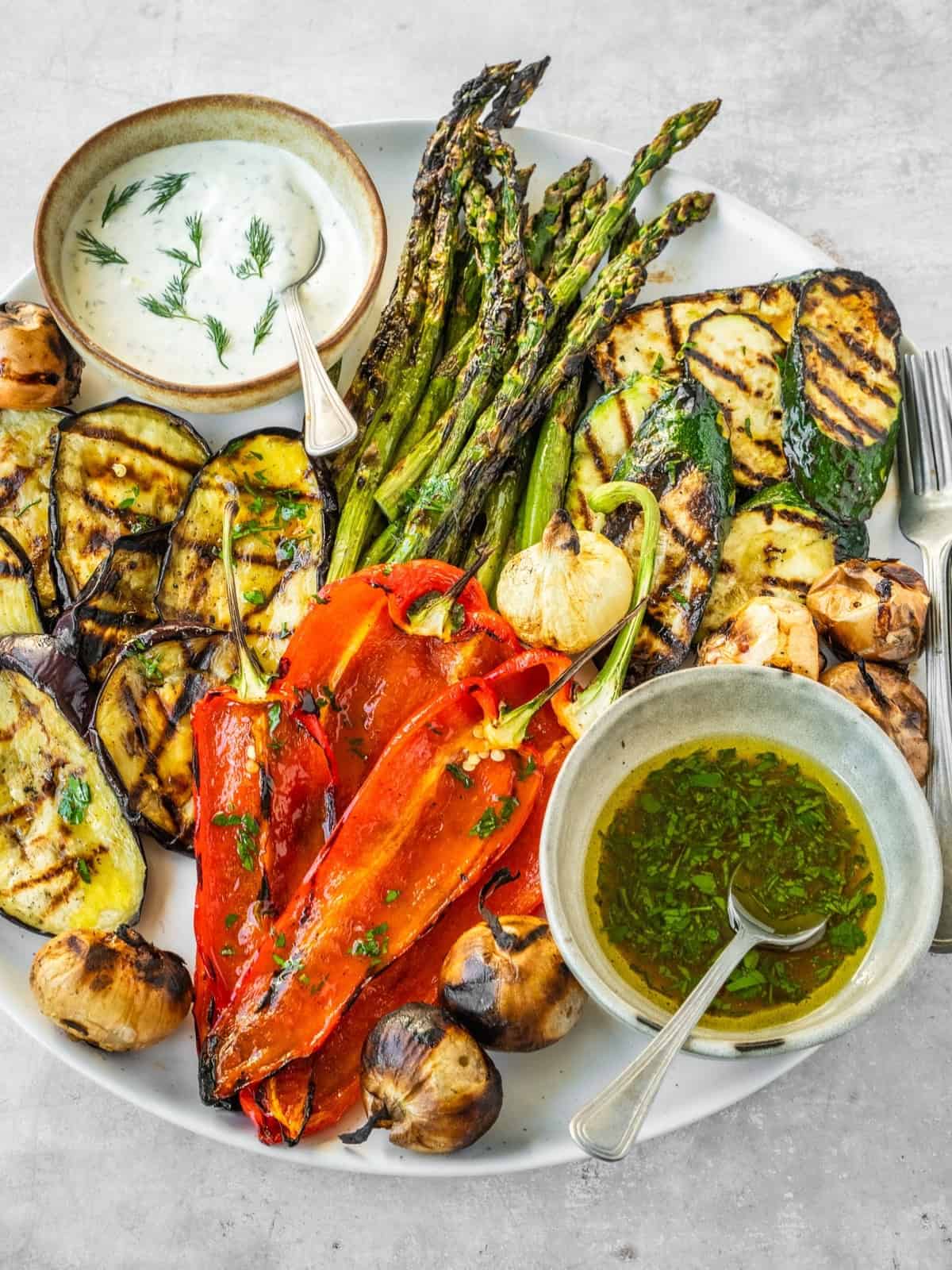 Grilled vegetables including asparagus, zucchini, eggplant and peppers on a platter with two sauces, one creamy and one oily.