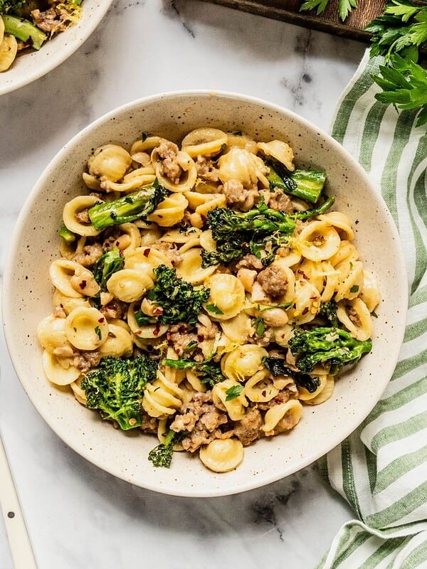 Creamy orecchiette with sausage, broccolini, and white beans in a bowl with chili flakes and parmesan garnish.