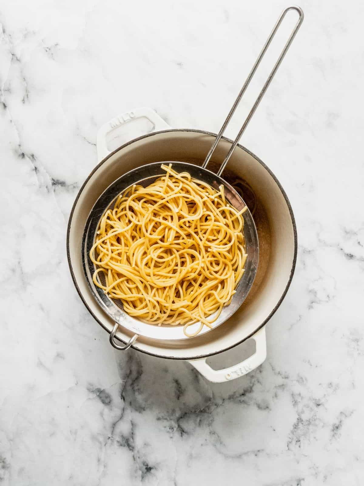 Spaghetti pasta draining in a sieve over a pot.