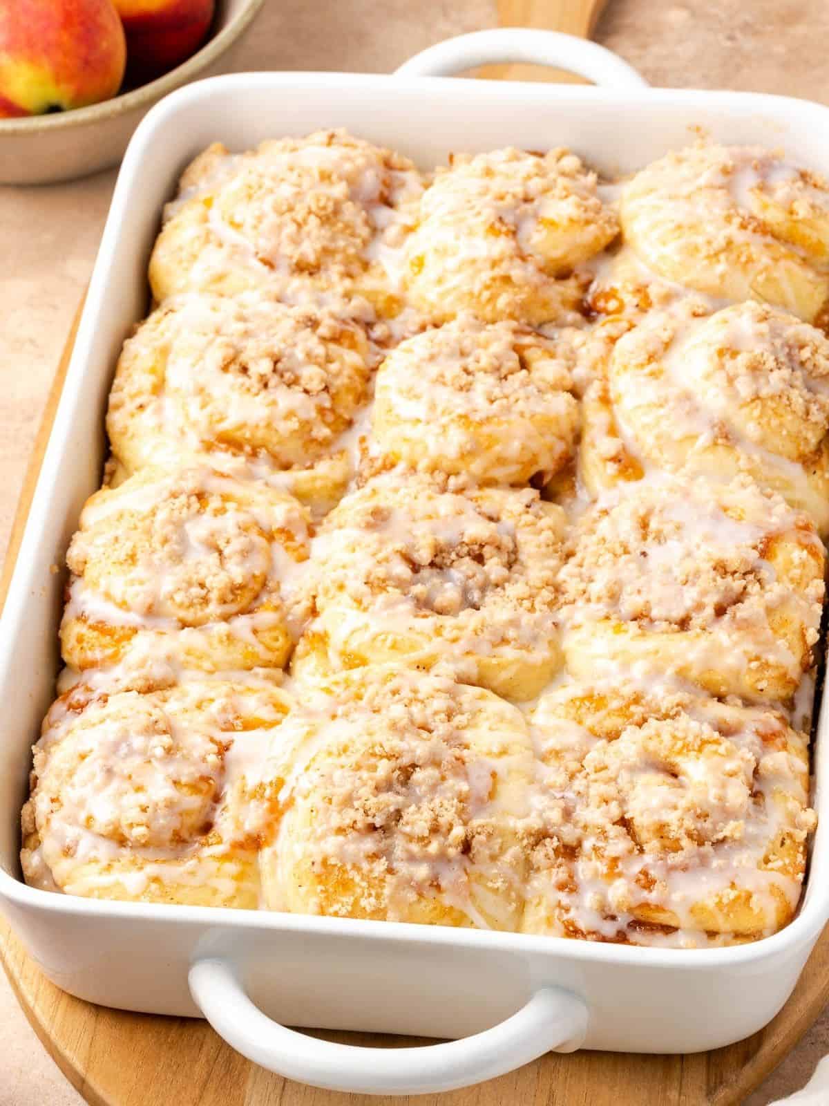 Peach cobbler cinnamon rolls in a baking dish, garnished with a simple icing.
