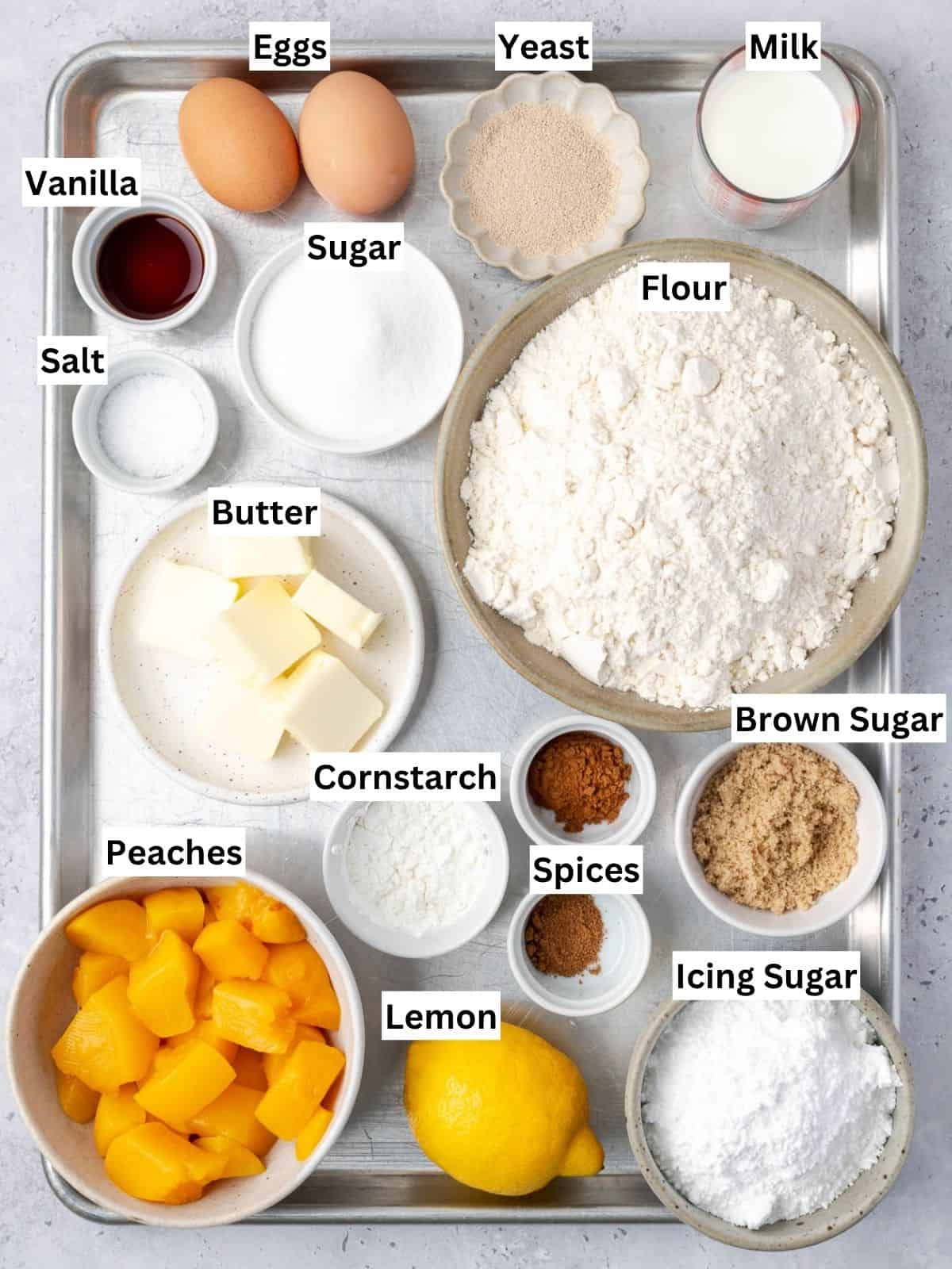 Peach cobbler cinnamon rolls recipe ingredients with individual labels on a metal tray.