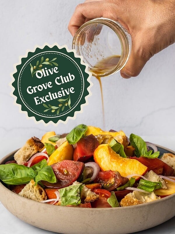 Drizzling dressing over a bowl of peach panzanella salad with chunky tomatoes, basil, croutons and shallots.