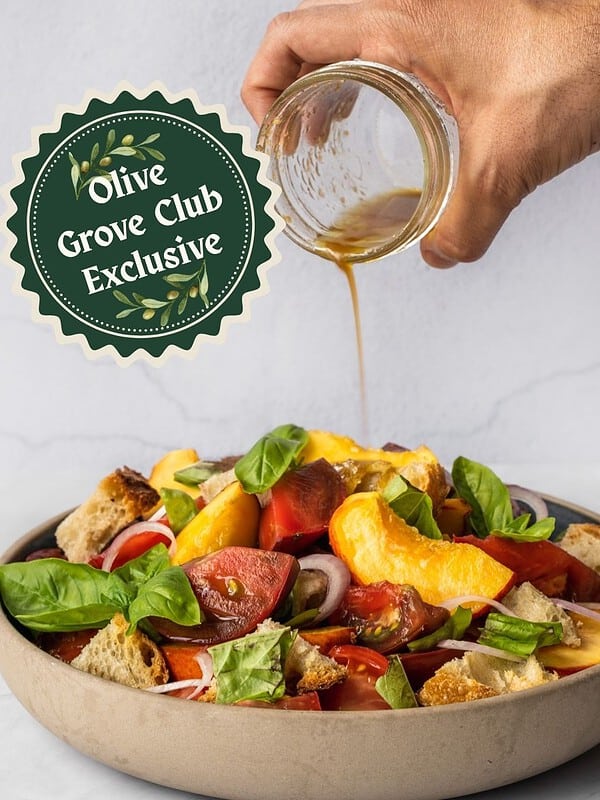 Drizzling dressing over a bowl of peach panzanella salad with chunky tomatoes, basil, croutons and shallots.