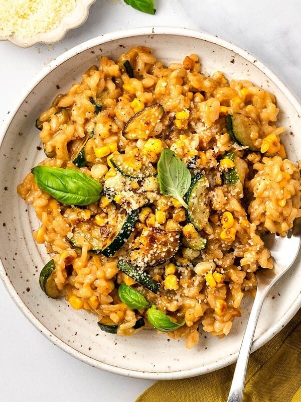 Summer risotto with squash and corn in a bowl garnished with fresh basil leaves.