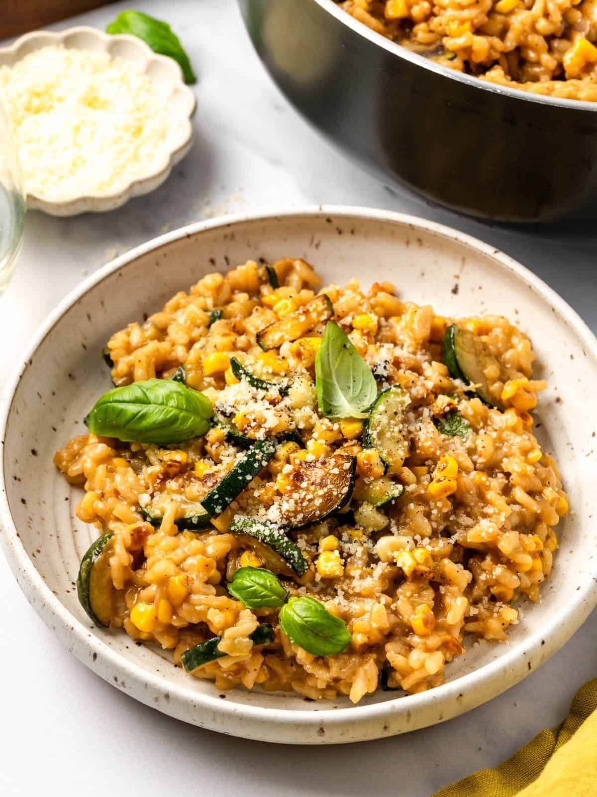 Summer risotto with squash and corn in a bowl garnished with fresh basil leaves.