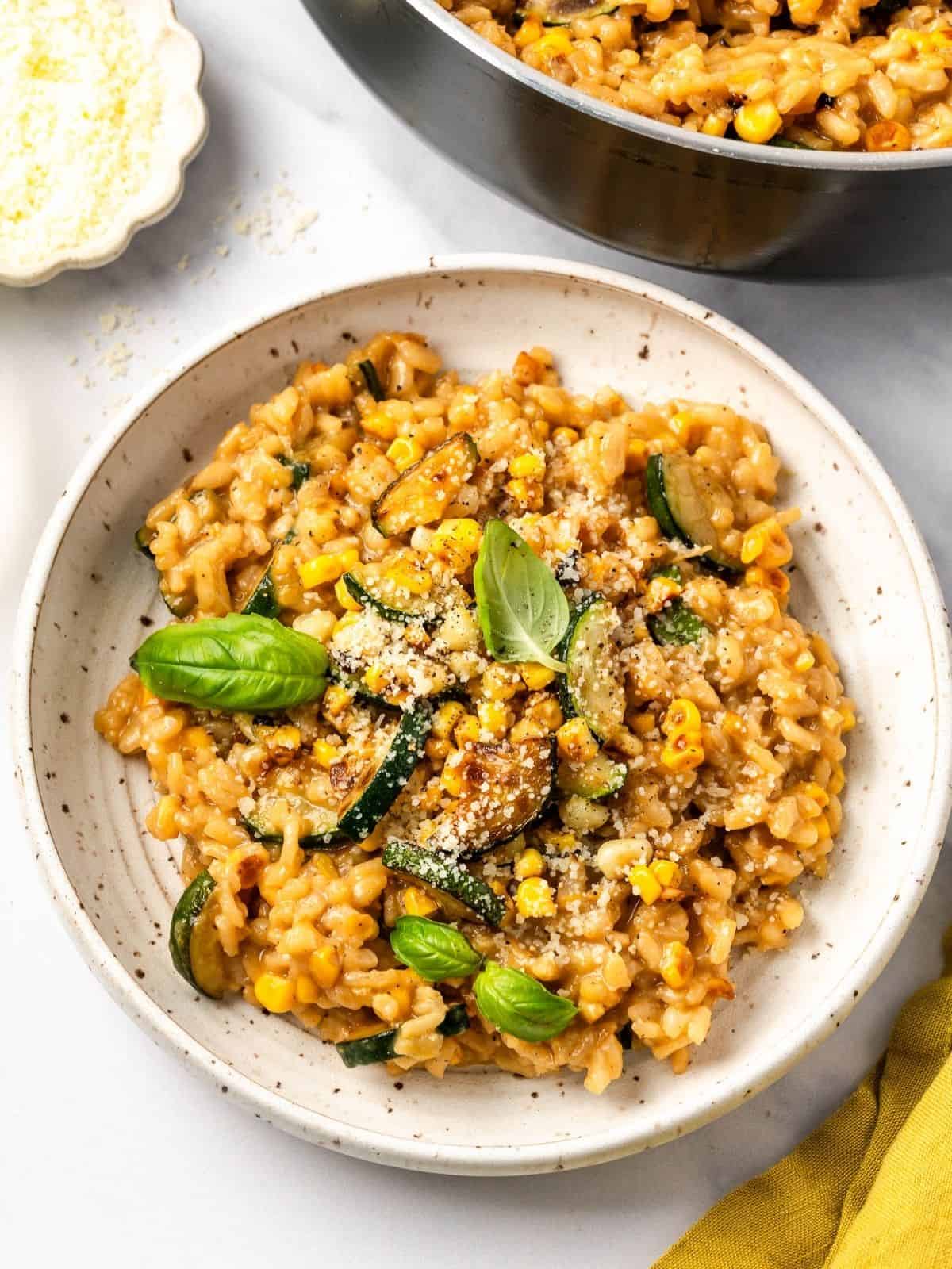 Summer risotto with squash and corn in a bowl garnished with fresh basil leaves.