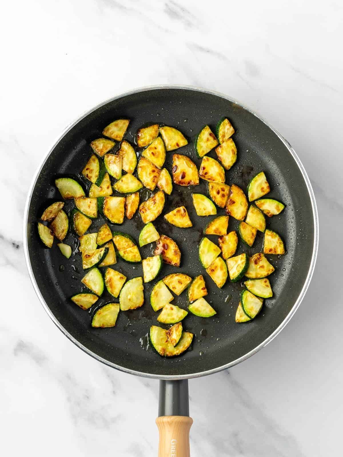 Recipe step showing the zucchini getting fried in a pan.