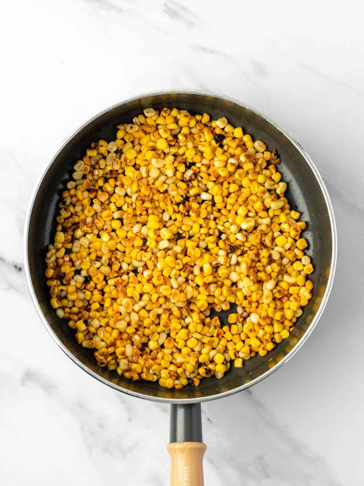 Recipe step showing the corn getting fried in a pan.