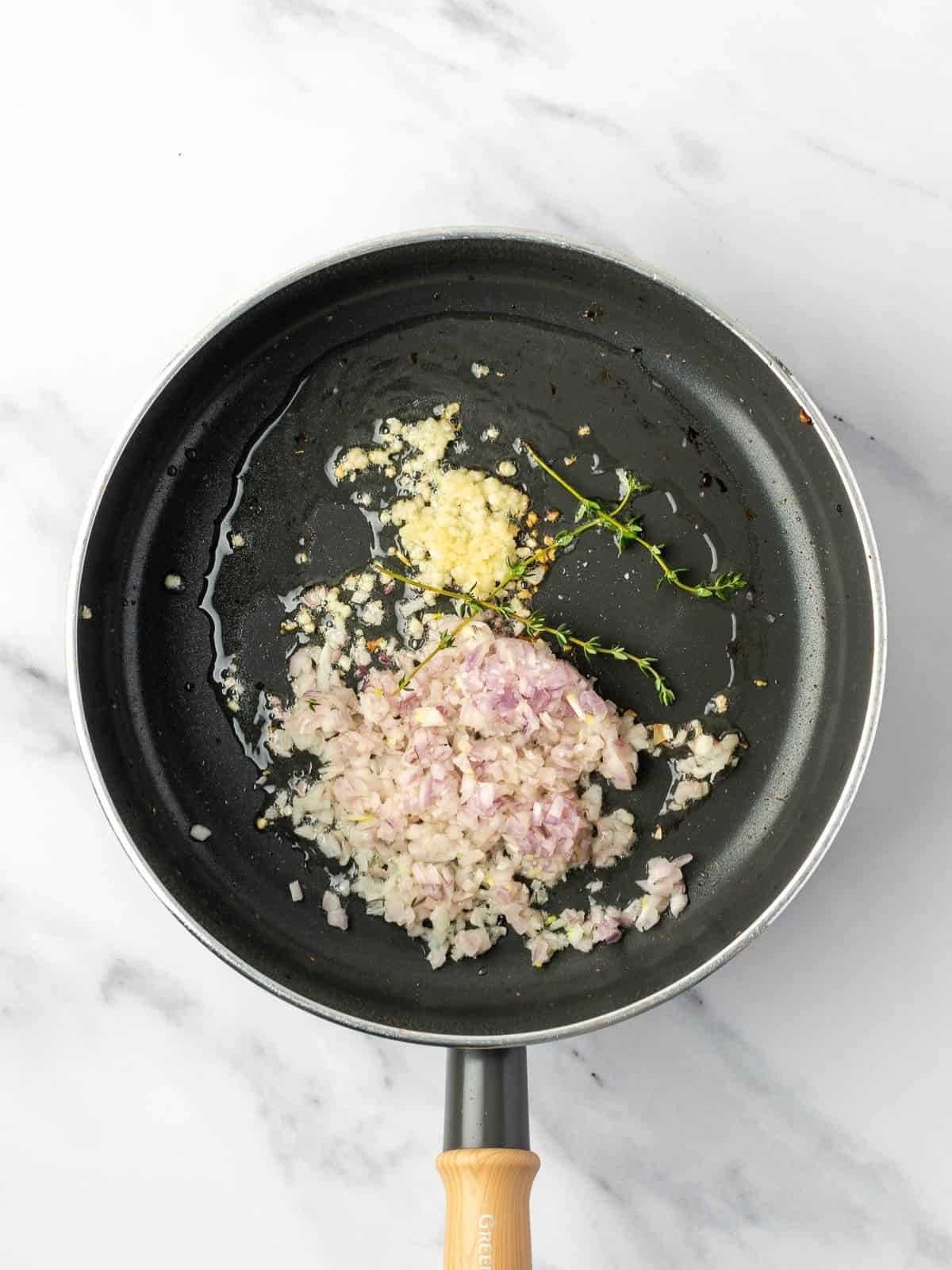 Recipe step showing the shallot, garlic, and thyme getting sauteed in sauce pan.