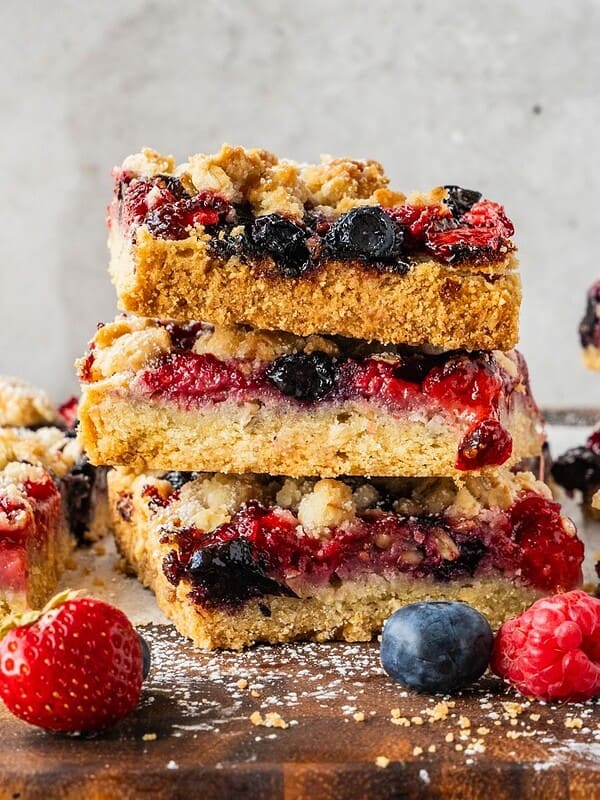 A stack of triple berry bars with oatmeal shortcrust on a wooden board.