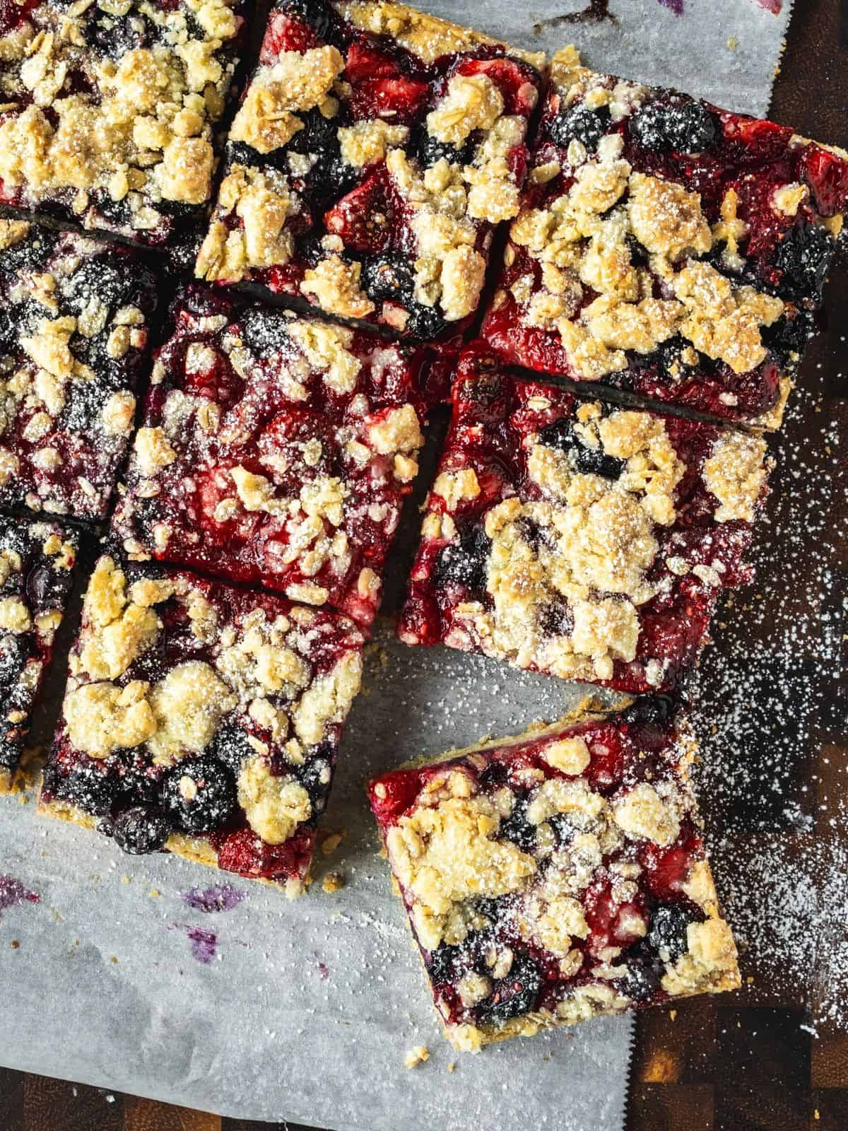 Slices of triple berry bars with oatmeal shortcrust on a wooden board.
