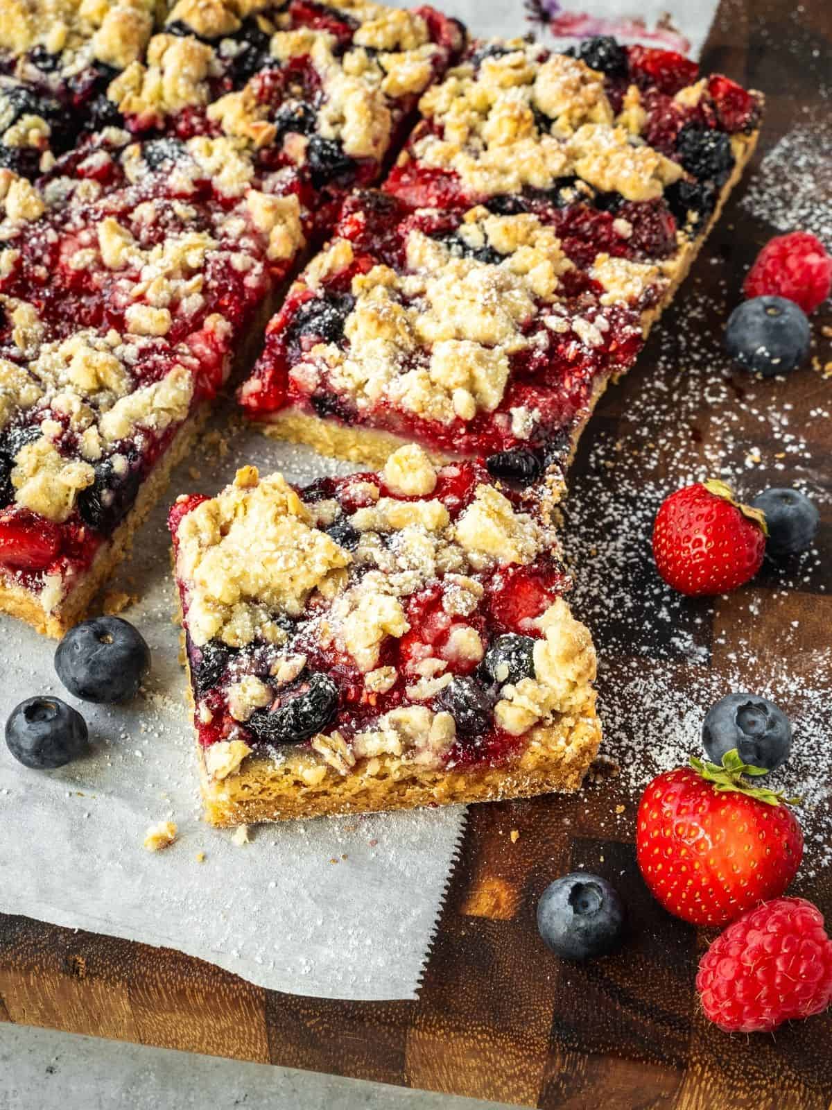 Slices of triple berry bars with oatmeal shortcrust on a wooden board.