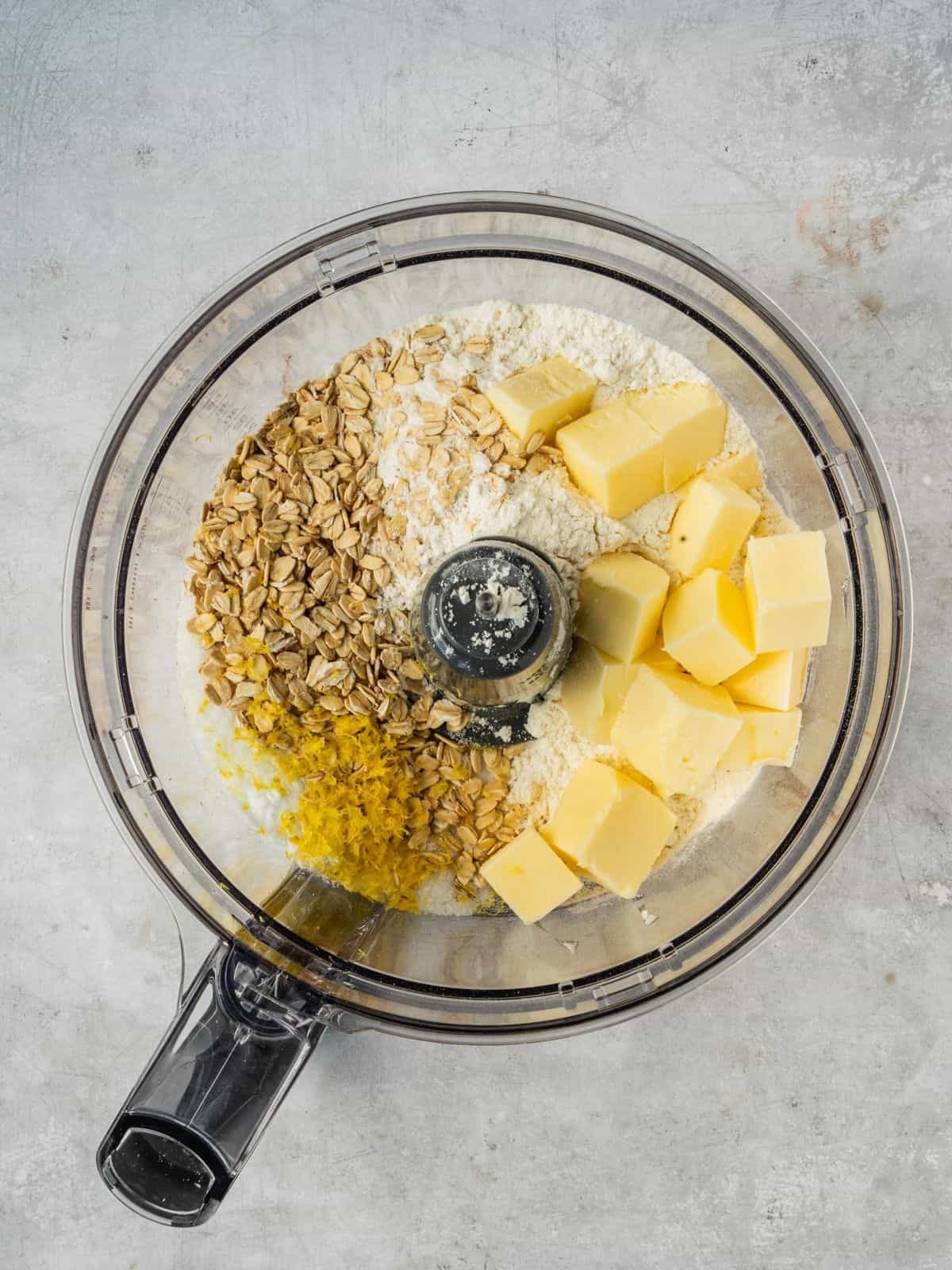 Flour, oats, butter, sugar, lemon zest, salt, and baking soda in the bowl of a food processor.