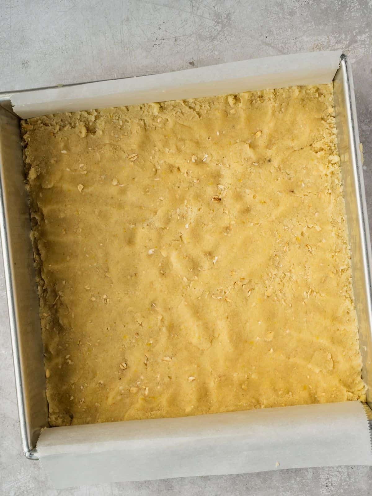 Shortcrust pressed into a parchment paper-lined square metal baking tray.