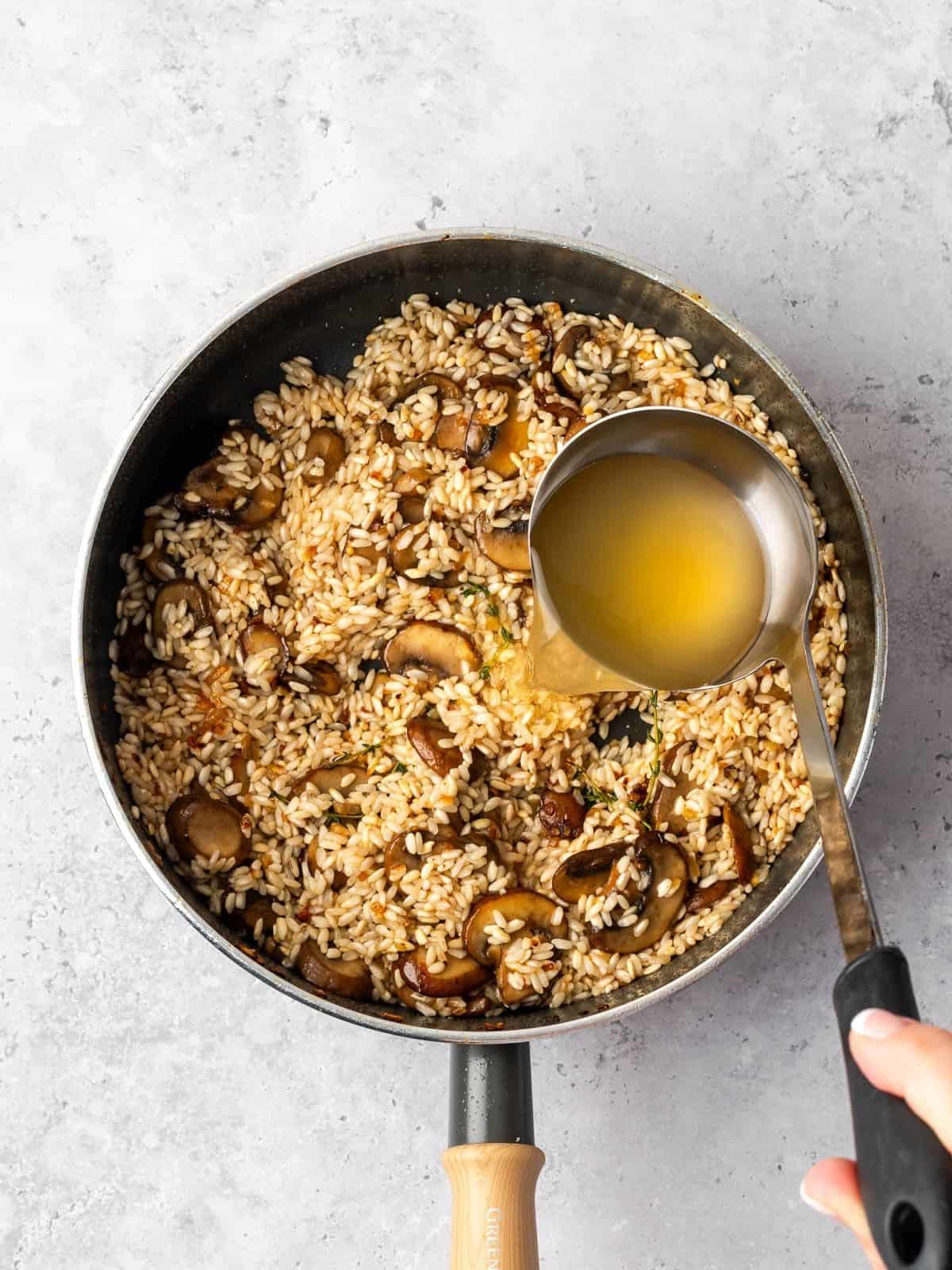 Ladling chicken broth over the simmering arborio rice and mushrooms.