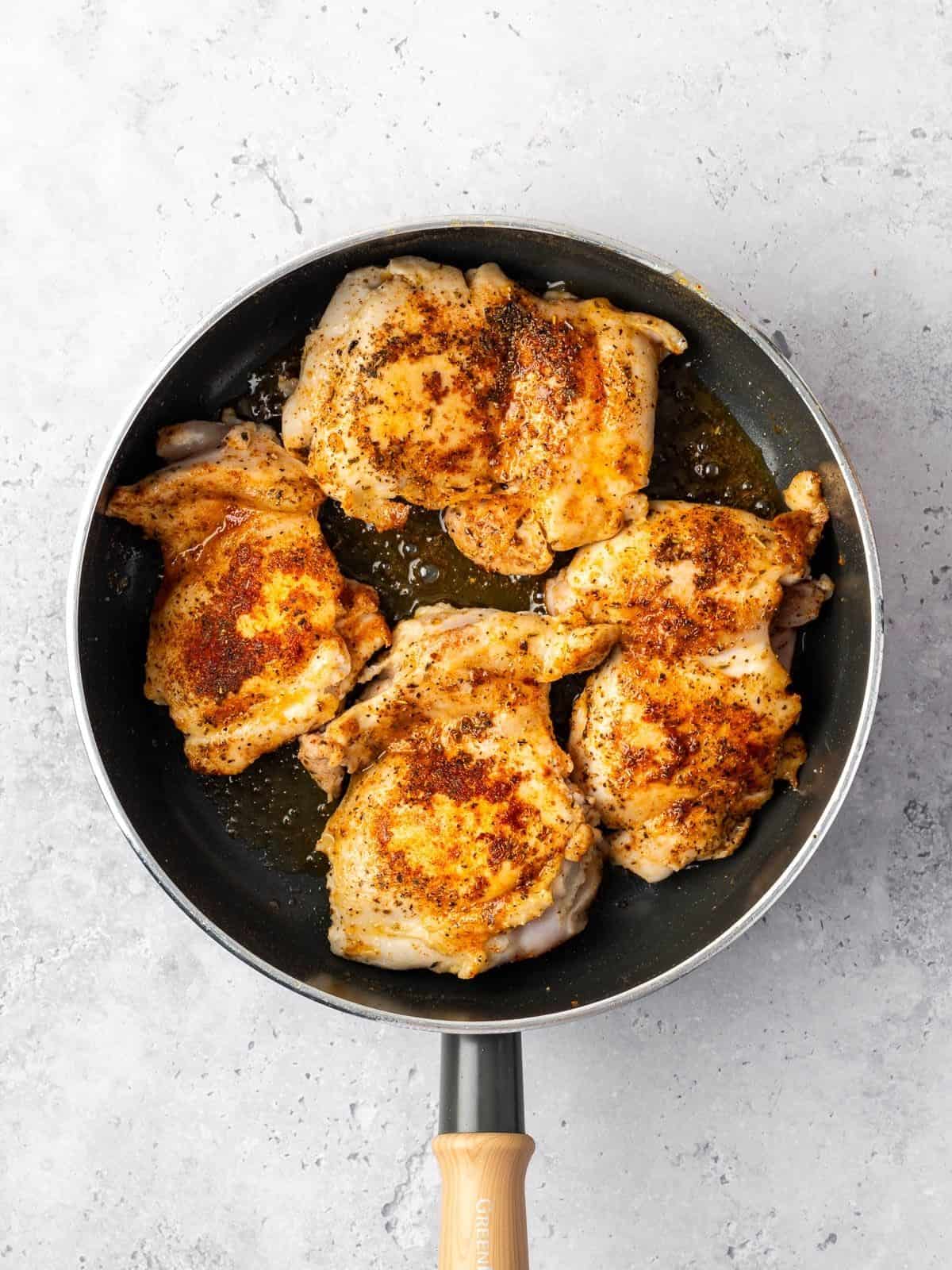 Seasoned chicken thighs frying in a sauté pan.
