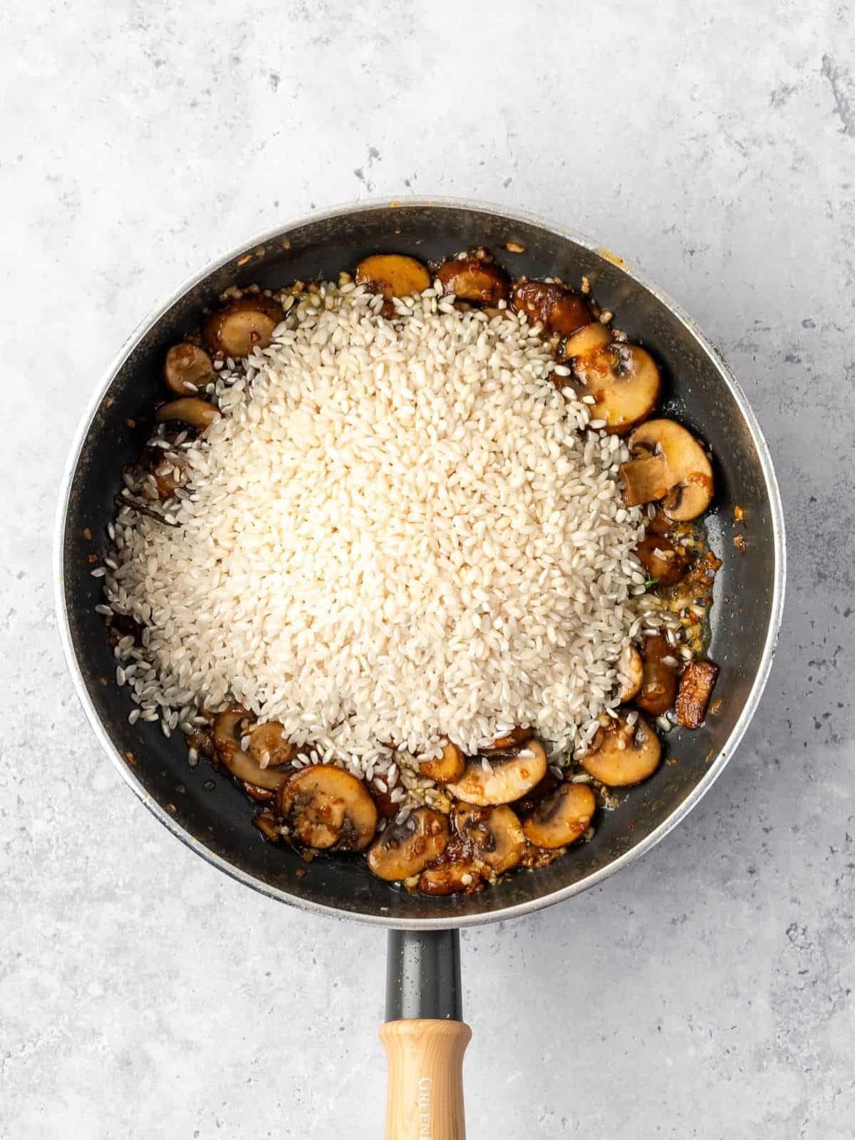 Adding rice to the cooked mushrooms and aromatics to toast.