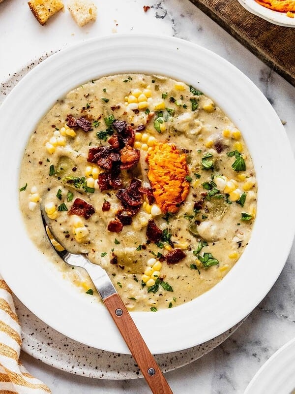Bowl of corn chowder with harissa butter, bacon and fresh herbs.