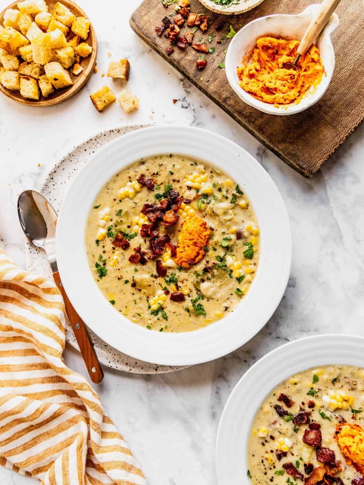 Bowls of corn chowder with harissa butter, bacon and fresh herbs.
