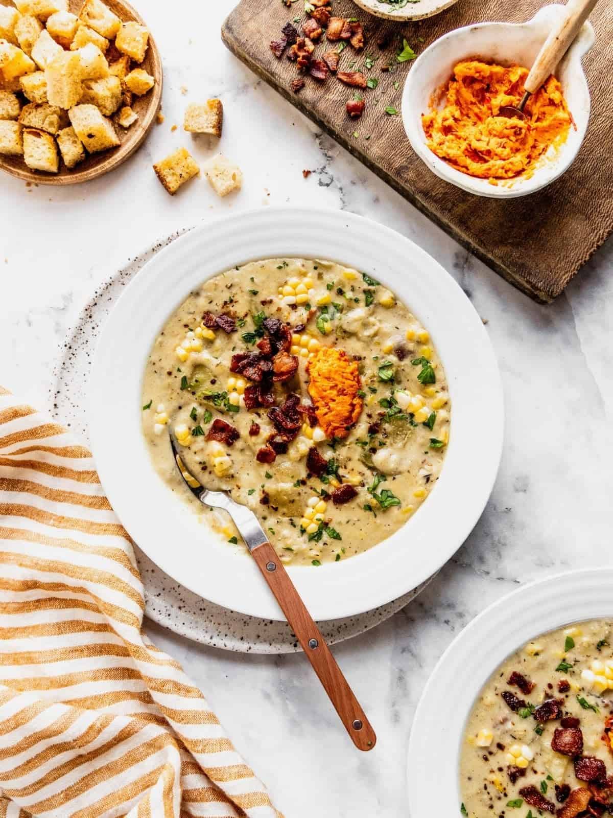 Bowls of corn chowder with harissa butter, bacon and fresh herbs.
