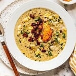 Bowl of corn chowder with harissa butter, bacon and fresh herbs.