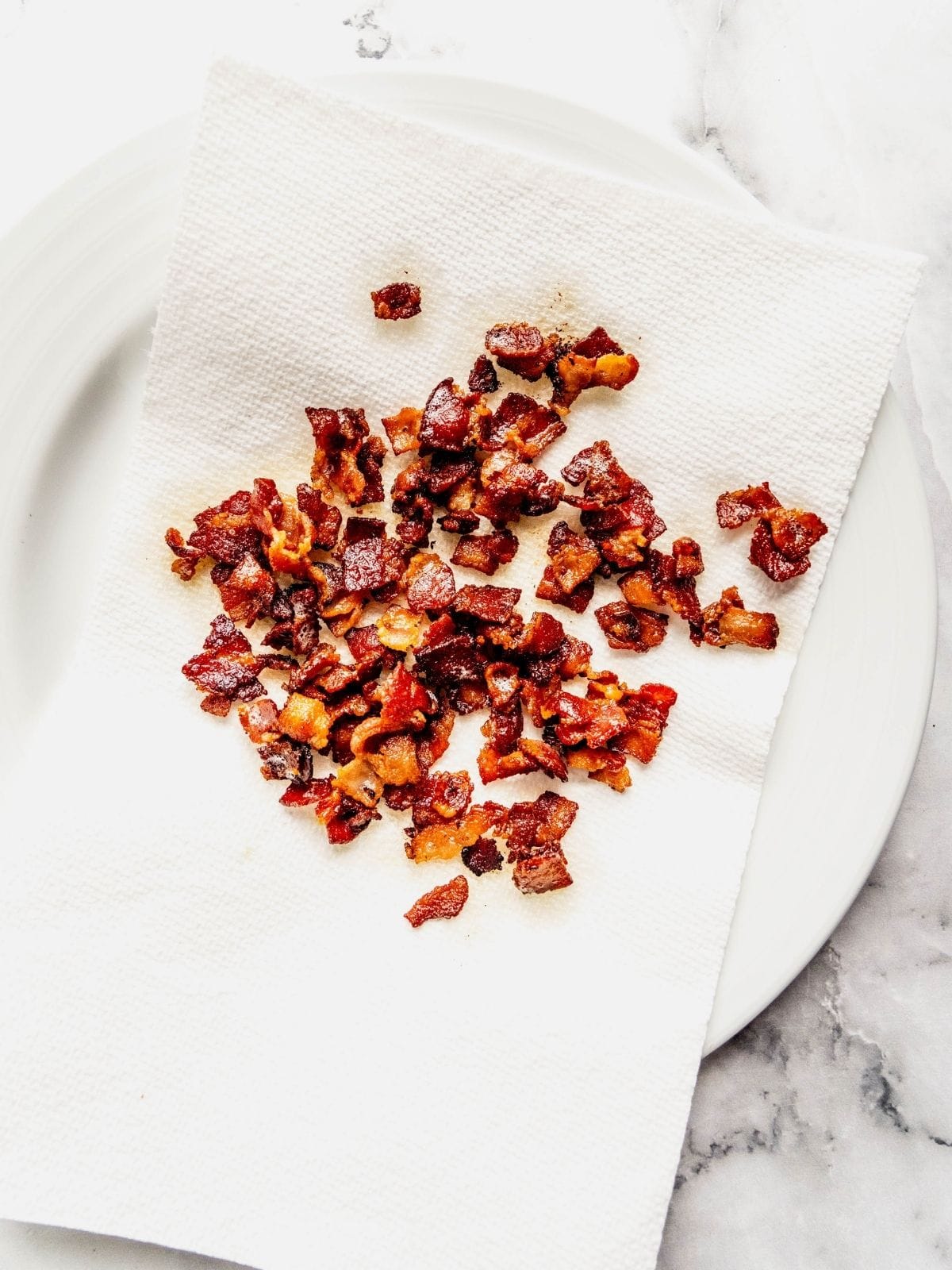 Fried bacon bits draining on a plate lined with paper towel.