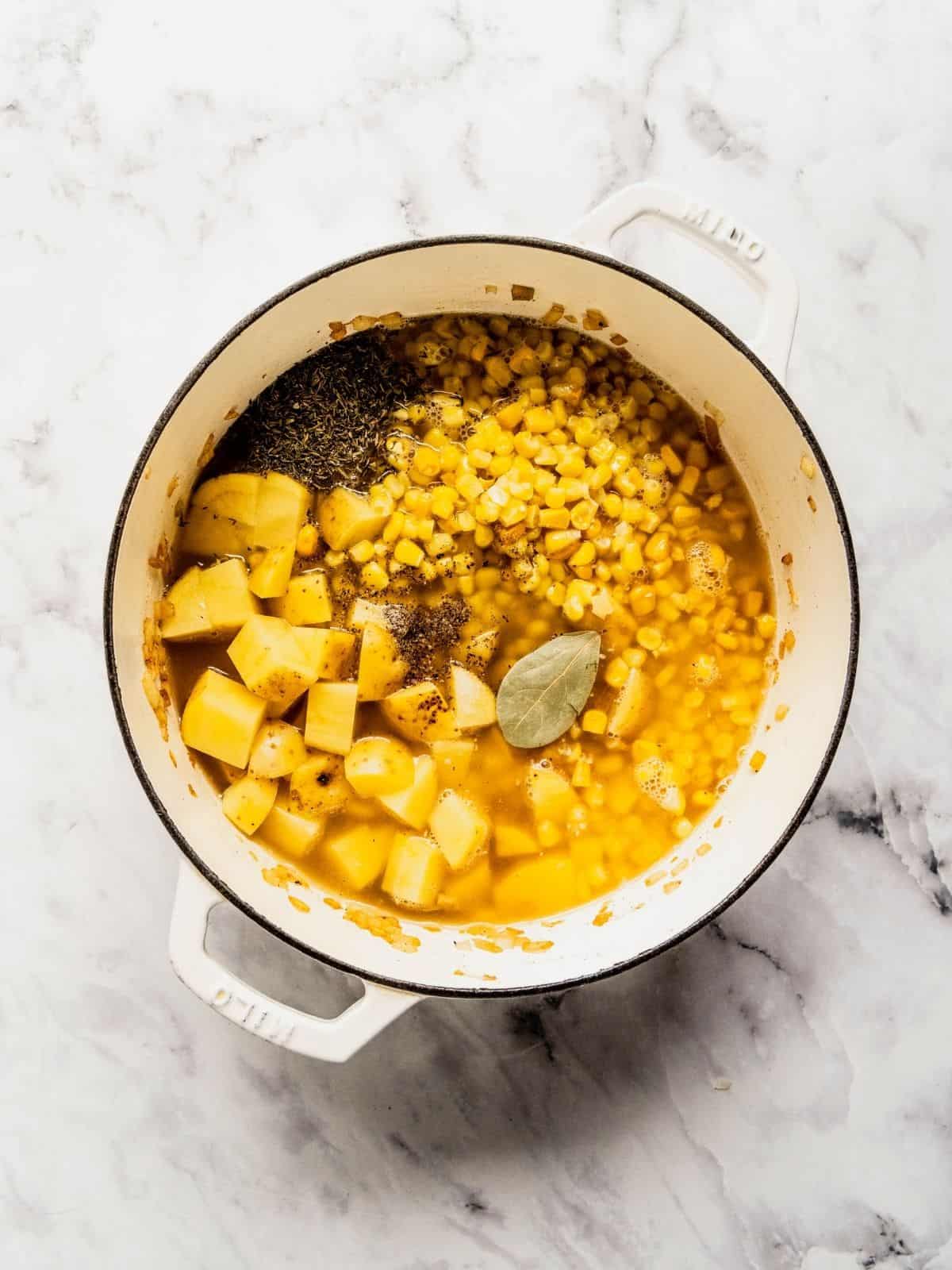 Potatoes, corn, spices and broth added to the soup pot.